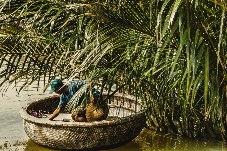 Fisherman in a round basket boat under nipa palms on a Mekong waterway